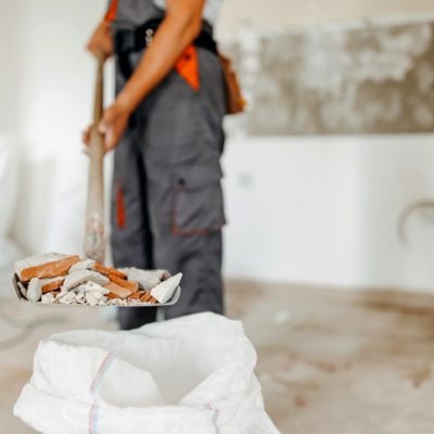 A cleaning professional shovels construction debris into a bag for removal.